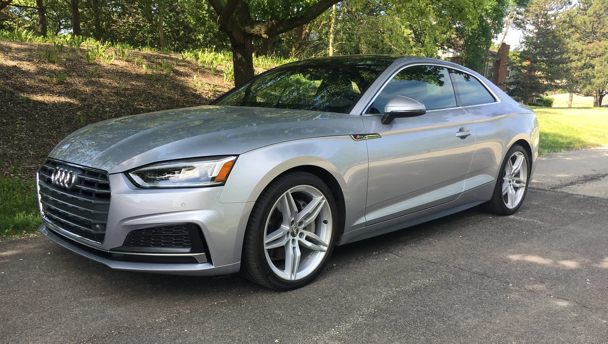 Silver Audi A5 coupe parked on a road, showcasing its sleek design and modern features.