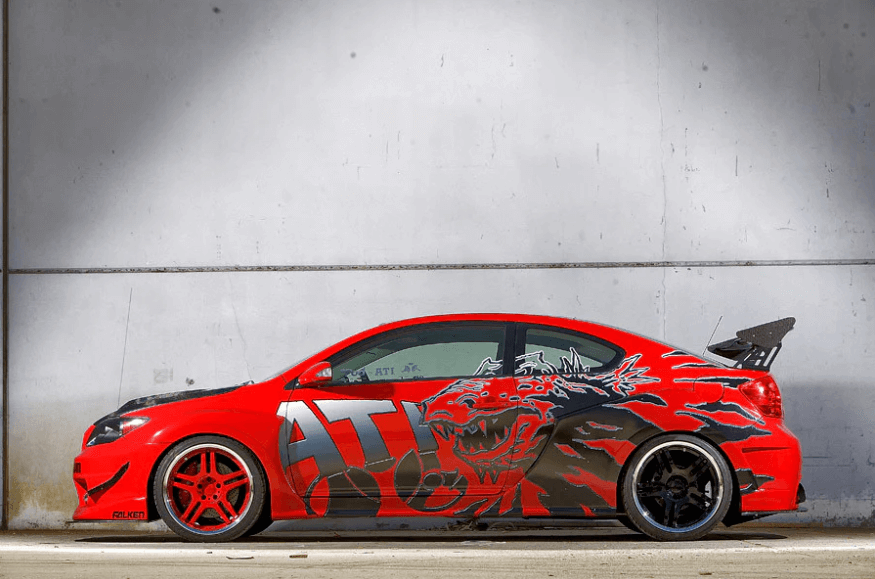 Modified red Scion tC with custom graphics and performance wheels, showcasing unique automotive design elements.