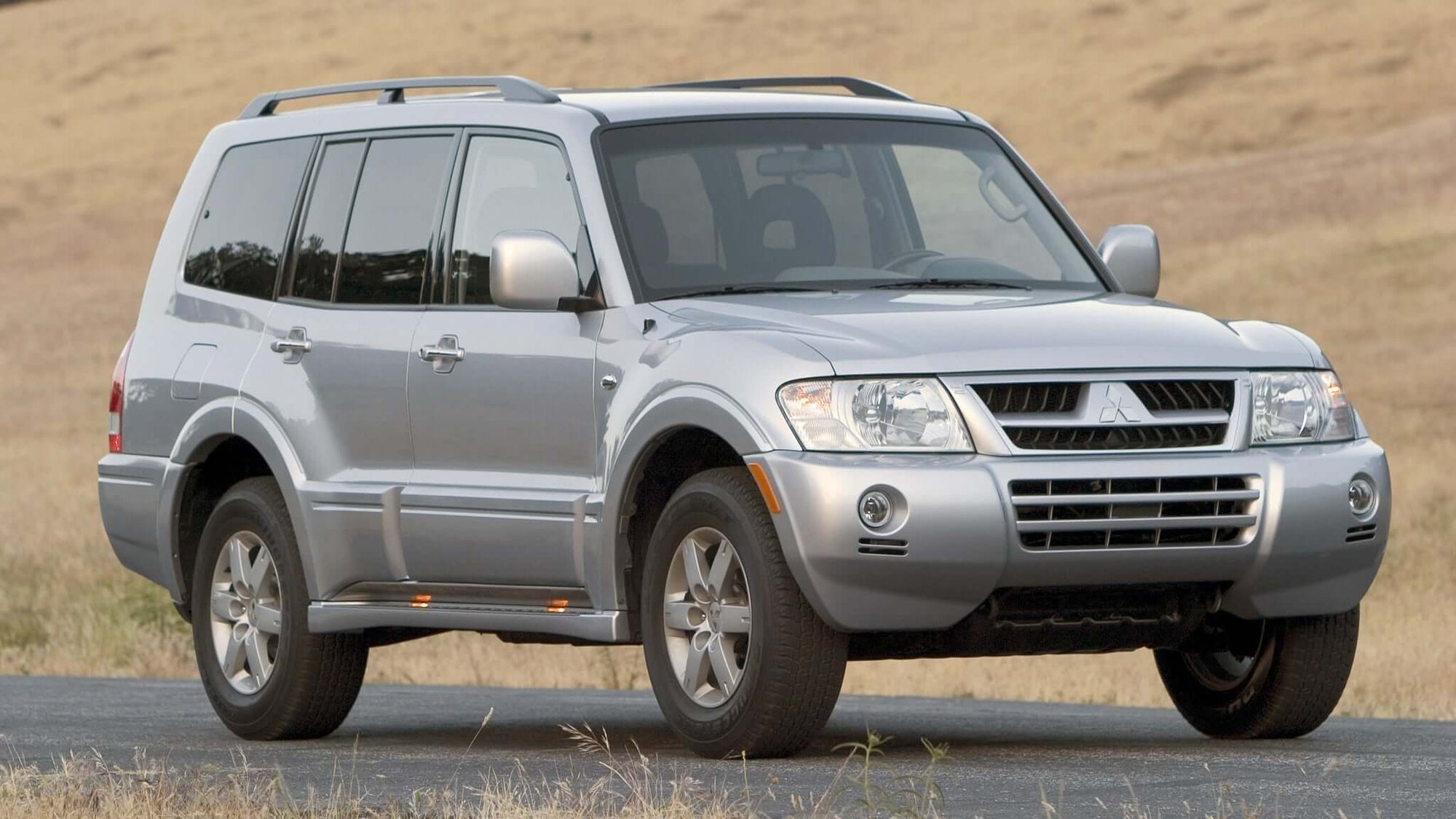 Silver Mitsubishi Montero (Pajero) parked by a grassy field, showcasing its robust SUV design.