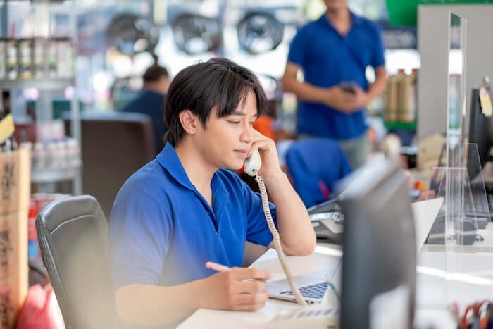 Young man in a blue shirt talking on the phone while working at a computer in a busy office.
