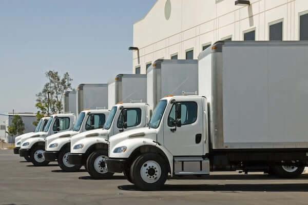 Row of white delivery trucks parked outside a warehouse ready for loading and transport.
