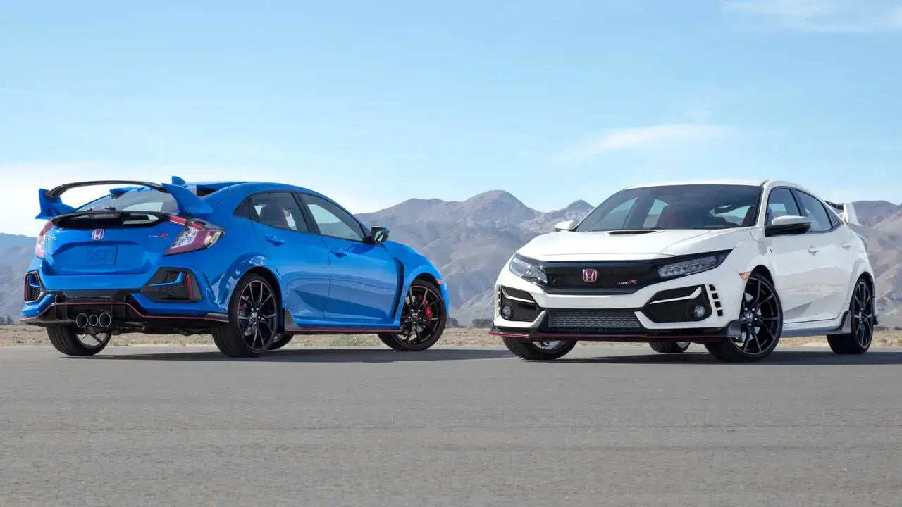 Two Honda Civic models in blue and white parked on a scenic road with mountains in the background.