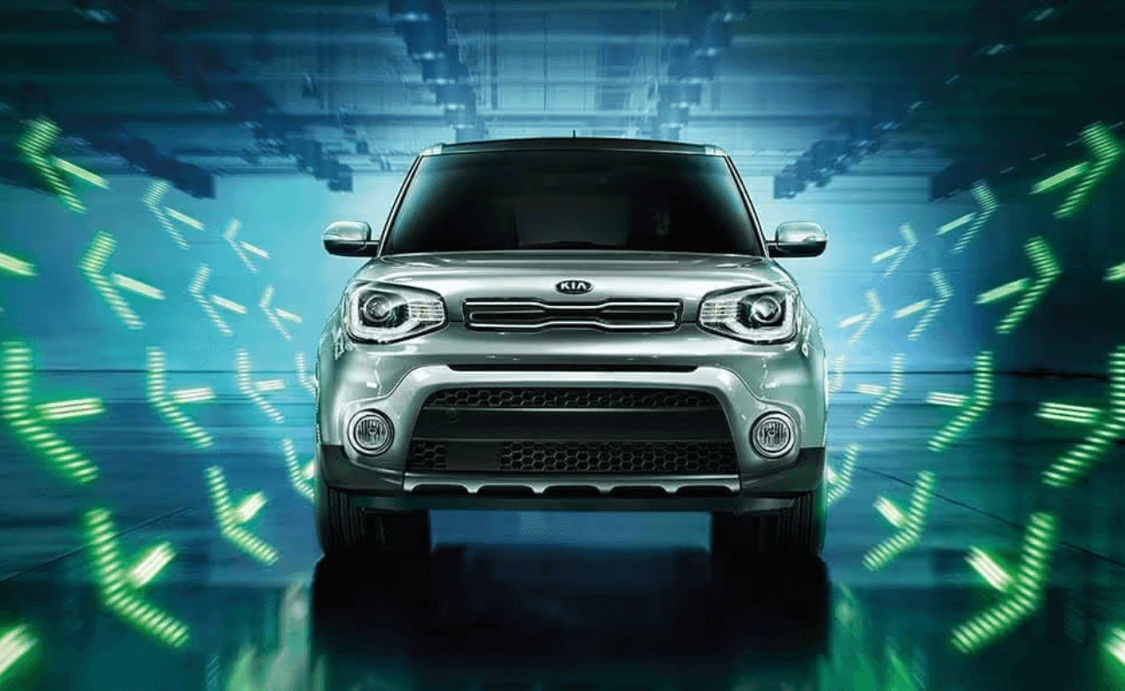 Front view of a silver Kia Soul surrounded by vibrant green arrow lights in a modern setting.