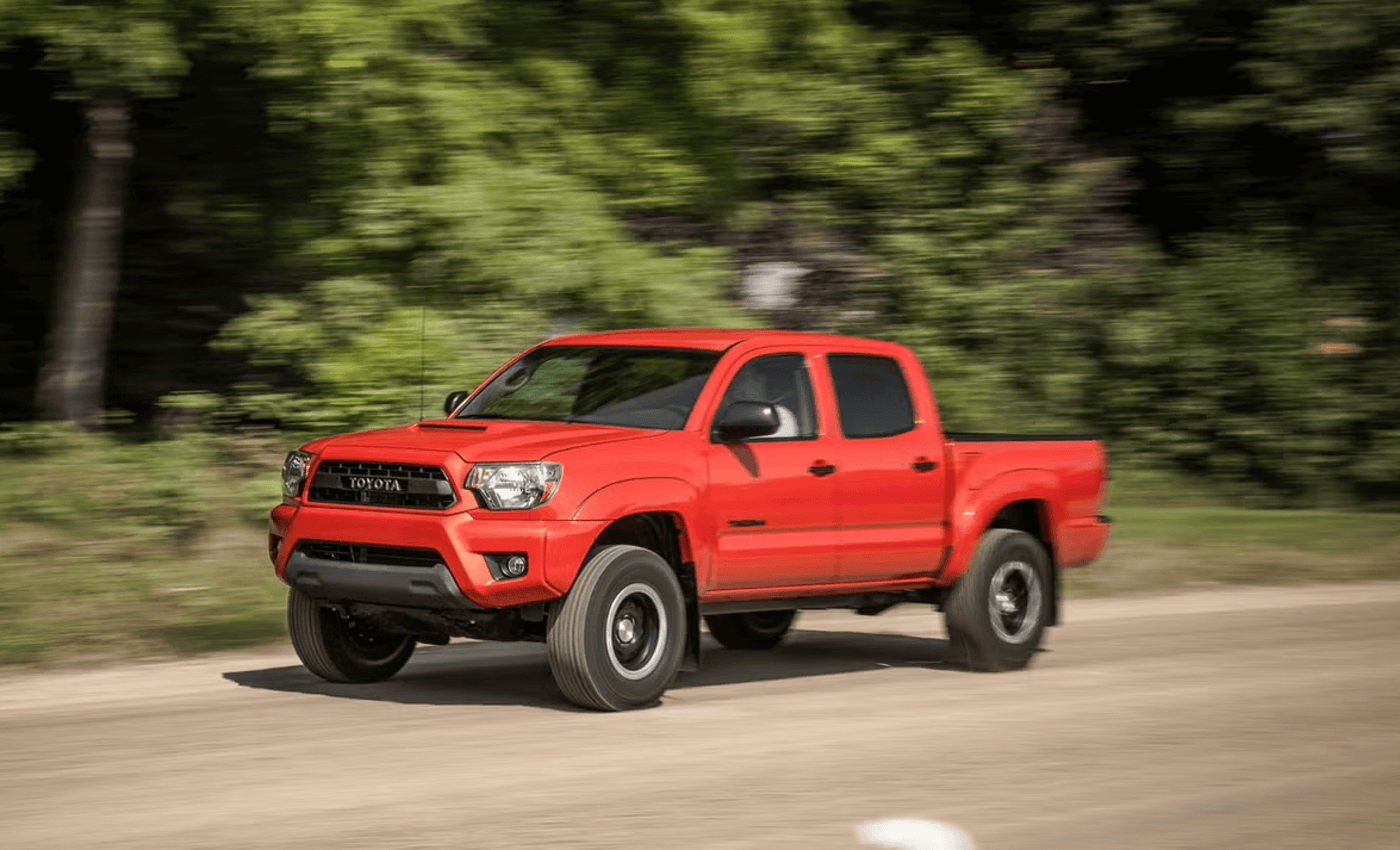 Red Toyota Tacoma truck driving on a dirt road surrounded by greenery.